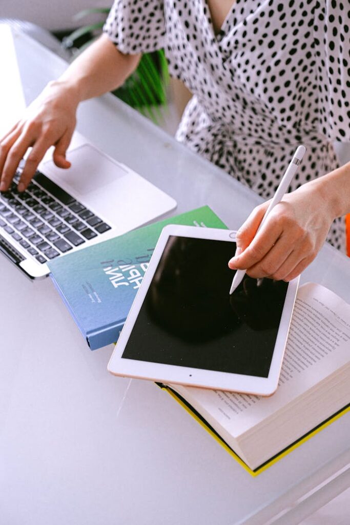 Woman multitasking with a laptop and tablet at a home office, showcasing remote work efficiency.